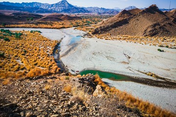A braided dry riverbed with residual pools running between arid mountains