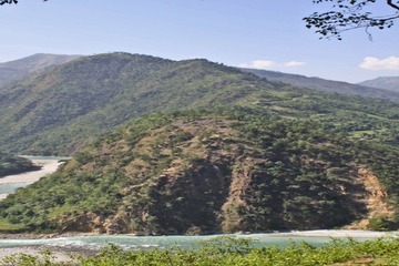 A Himalayan river winding through steep forested hills in Nepal, with terraced slopes and mountain ridges receding into haze.